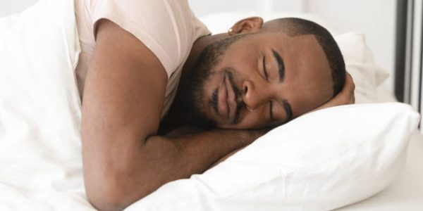 Serene calm handsome young black man sleeping well alone on orthopedic soft pillow under warm duvet, african american guy lying asleep in comfortable cozy bed enjoy good night peaceful healthy sleep